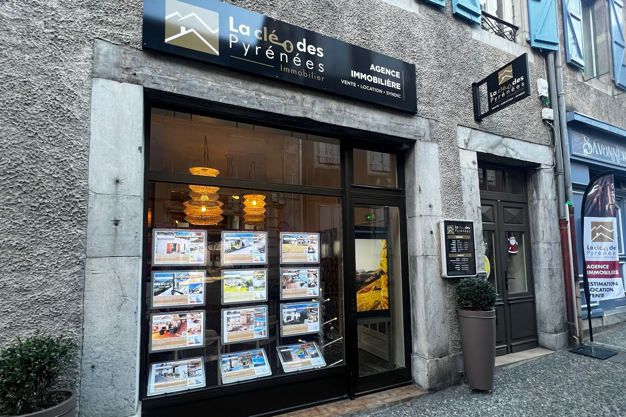 Devanture de l'agence immobilière La Clé des Pyrénées à Arreau, avec vitrine d'annonces éclairée
