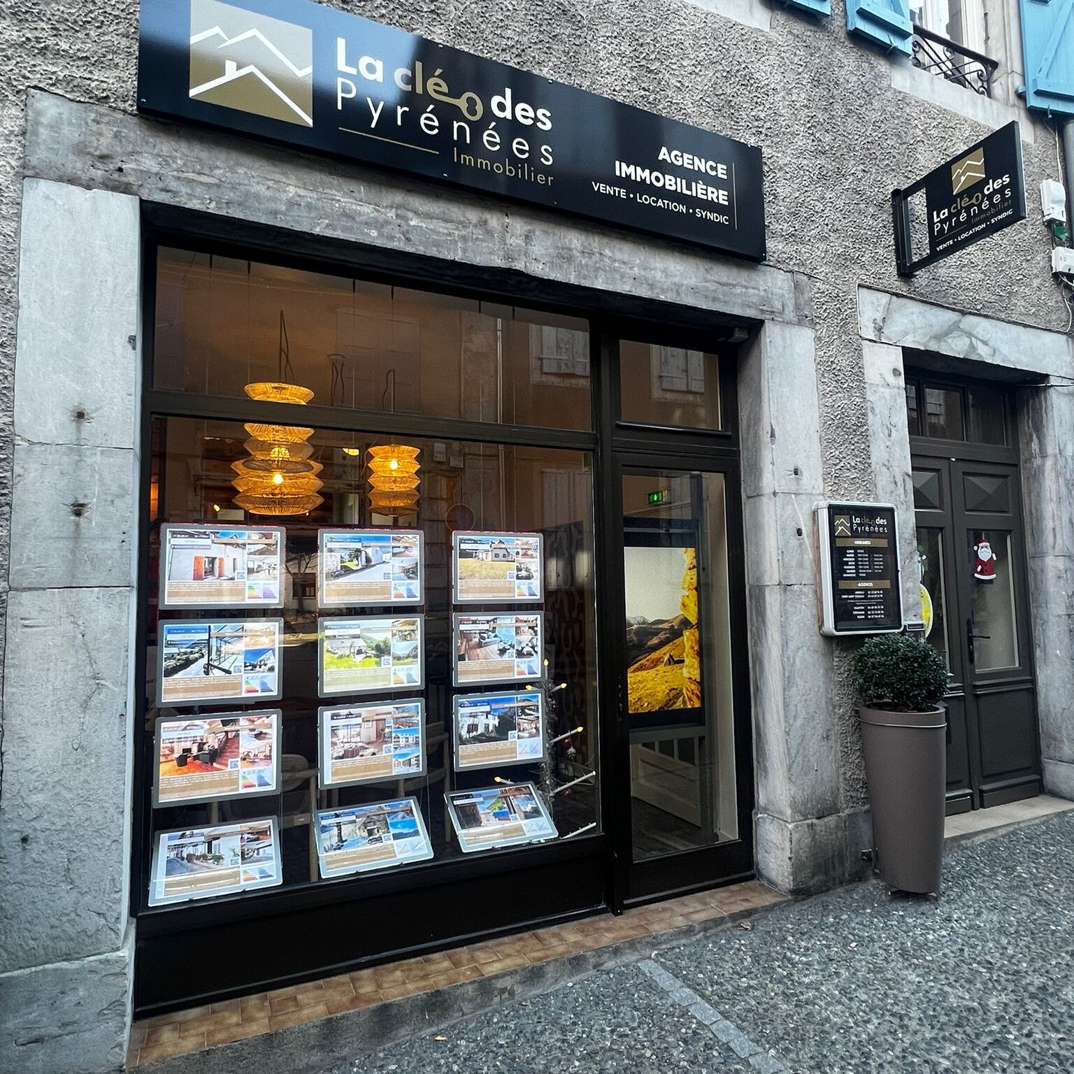Devanture de l'agence immobilière La Clé des Pyrénées à Arreau, avec vitrine d'annonces éclairée