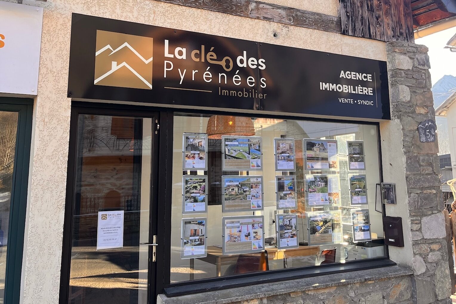 Devanture de l'agence immobilière La Clé des Pyrénées à Loudenvielle, façade en pierre avec vitrine d'annonces
