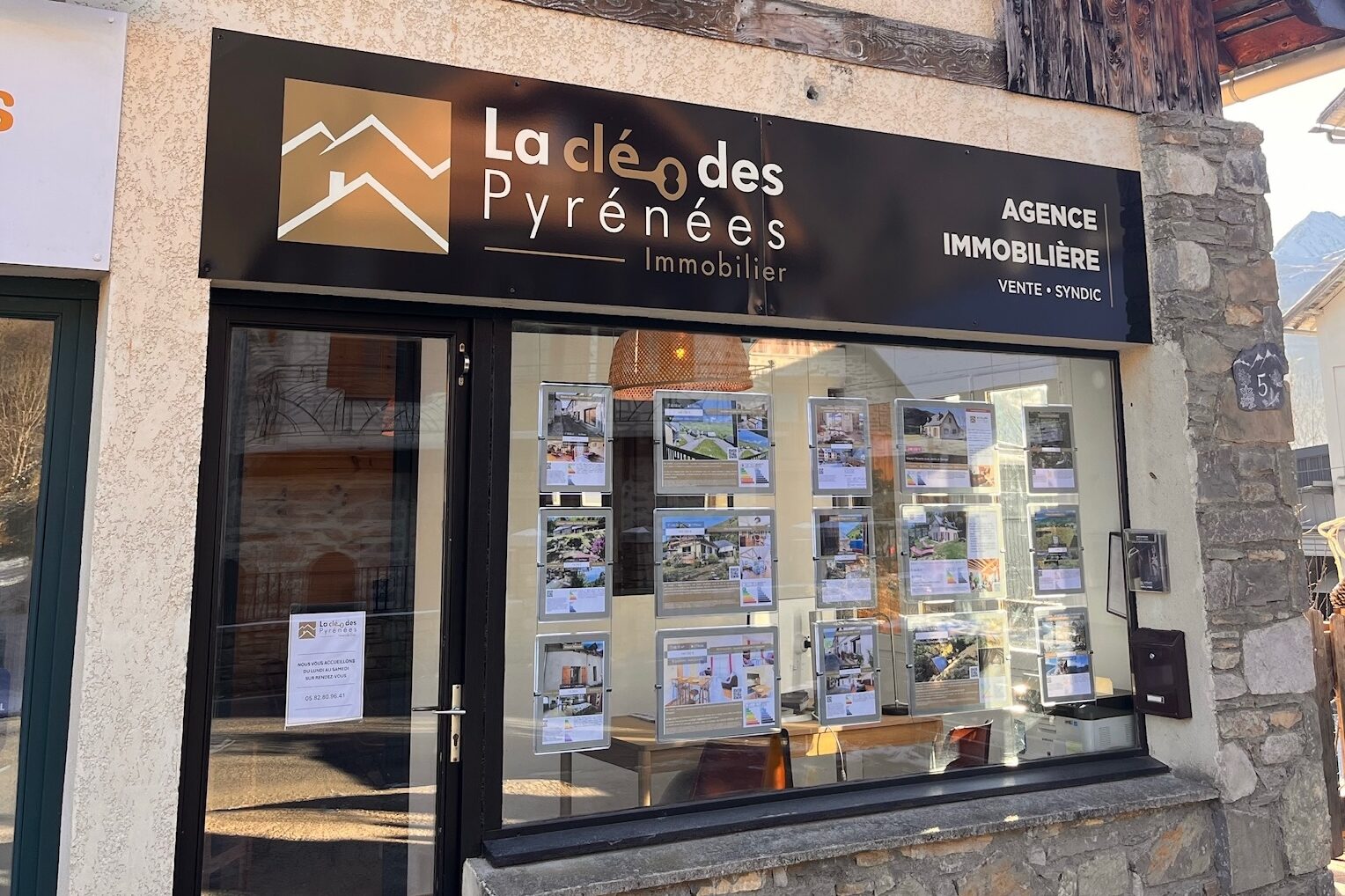 Devanture de l'agence immobilière La Clé des Pyrénées à Loudenvielle, façade en pierre avec vitrine d'annonces