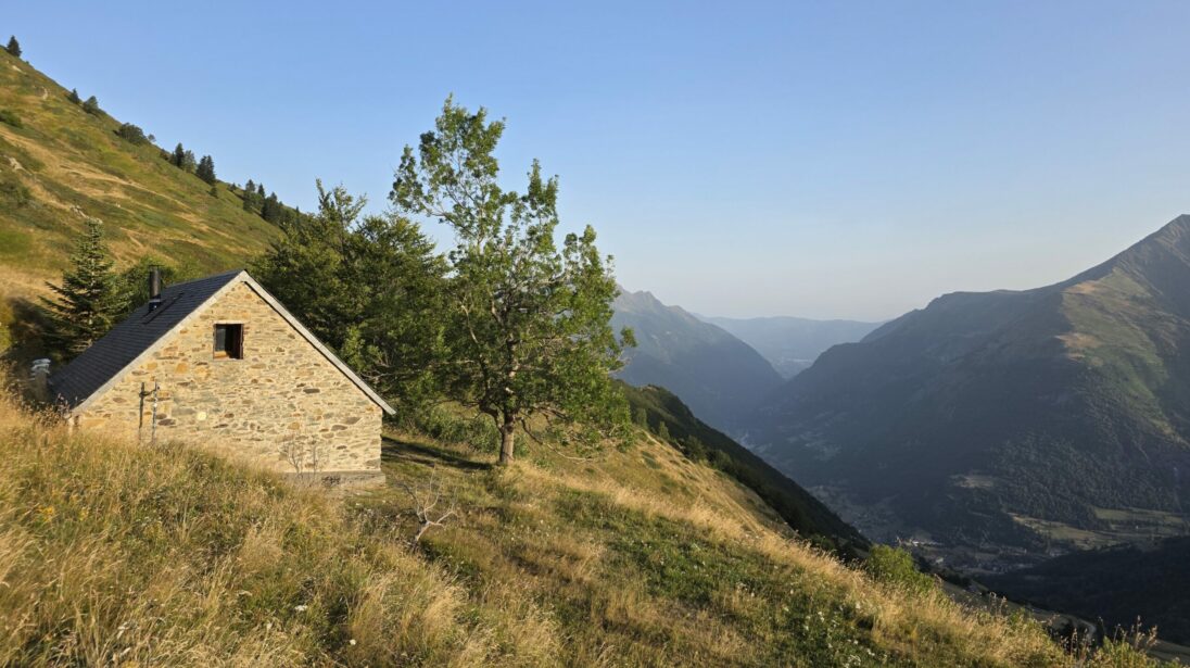 Grange foraine en pierre sur un versant herbeux surplombant une vallée pyrénéenne