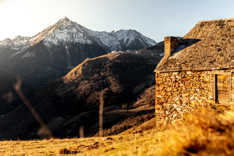 Façade en pierre d'une grange de montagne avec cheminée et toit en ardoise, sommets enneigés de Saint-Lary-Soulan en arrière-plan