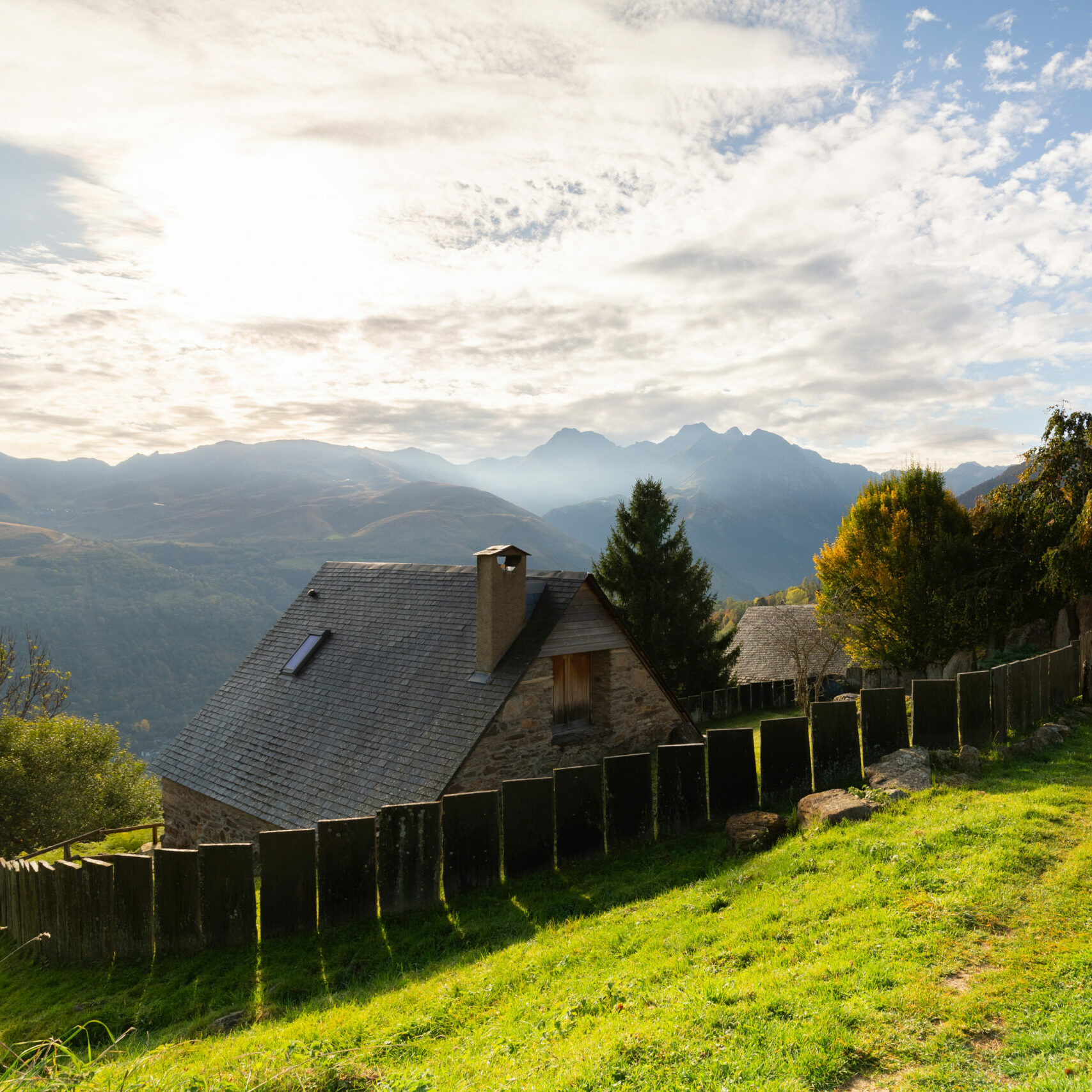 Granges en pierre entourées de prairies verdoyantes avec vue sur la vallée et les sommets pyrénéens au lever du jour