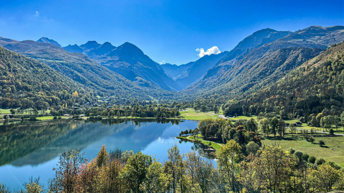 Vue sur le lac de Loudenvielle entouré de forêts avec le village et les sommets pyrénéens en arrière-plan