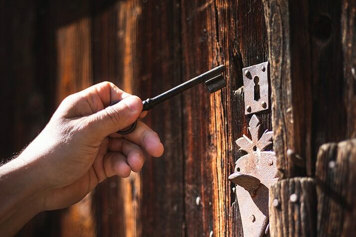 Main tenant une clé ancienne dans la serrure d'une porte en bois, symbole de La Clé des Pyrénées Immobilier