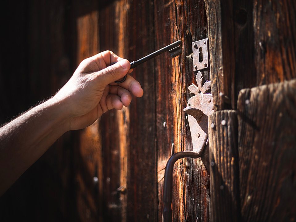 Main tenant une clé ancienne dans la serrure d'une porte en bois, symbole de La Clé des Pyrénées Immobilier
