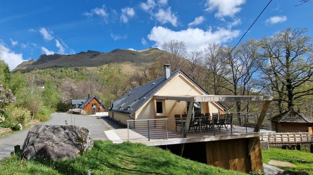 Maison de montagne avec grande terrasse en bois surélevée, jardin fleuri et sommets en arrière-plan dans les Hautes-Pyrénées