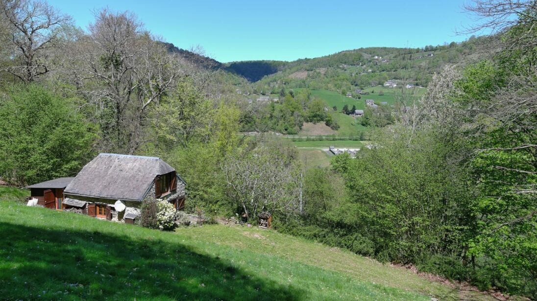 Maison de montagne avec toit en ardoise nichée dans un vallon verdoyant, vue sur un village de la vallée des Gaves