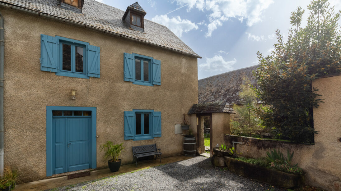 Maison de village pyrénéenne avec façade crépie et volets bleus, cour gravillonnée à Vielle-Aure