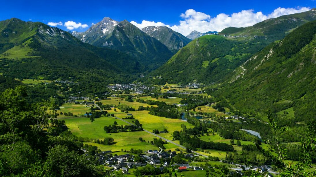 Panorama sur une vallée verdoyante avec village en fond de vallée, rivière et sommets environnants