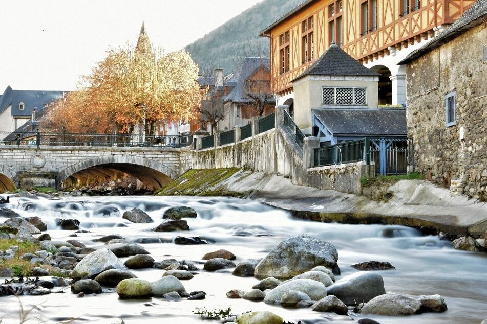 Pont en pierre ancien et mairie d'Arreau à colombages au bord de la rivière en automne