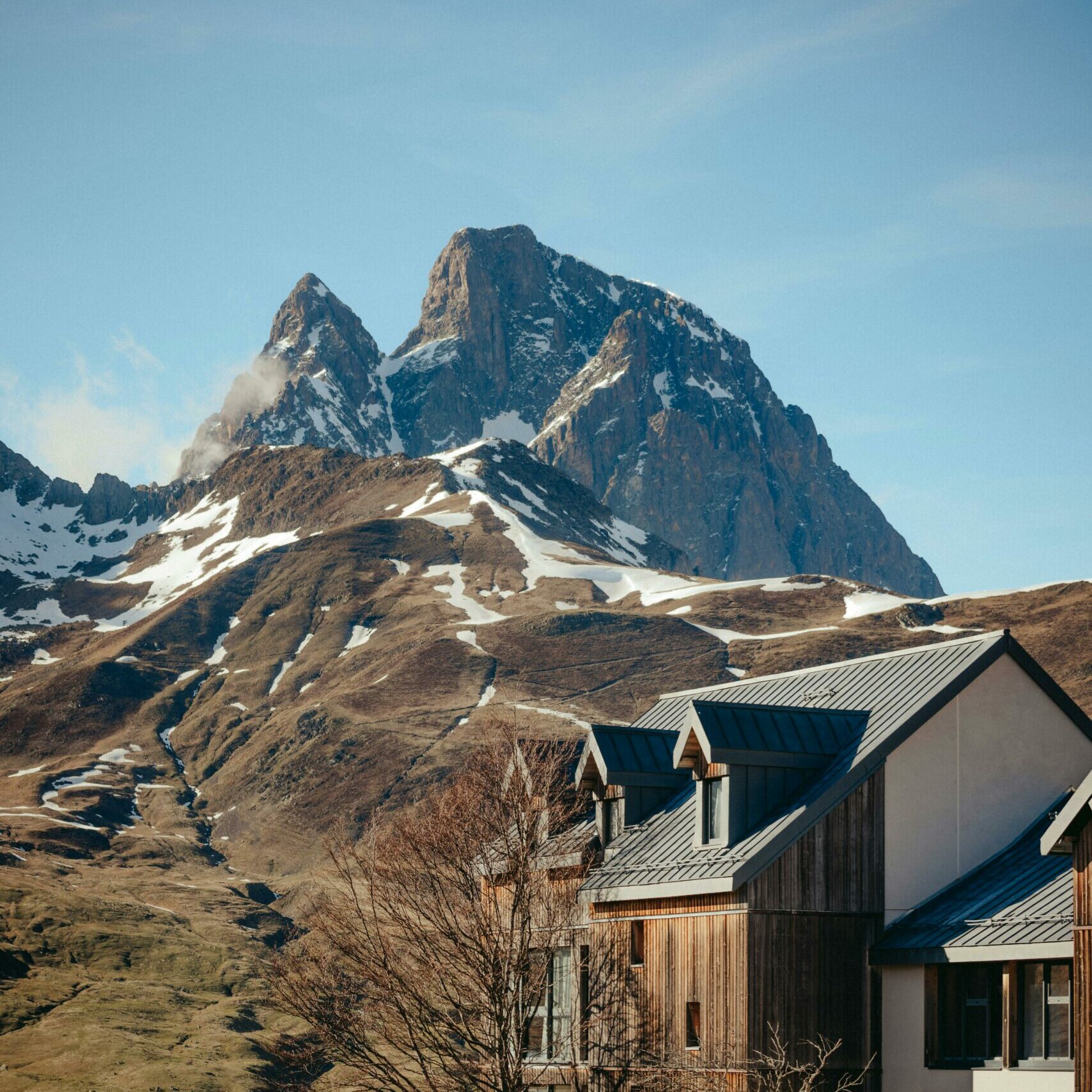 Résidence moderne en bois et crépi blanc au pied d'un sommet rocheux enneigé dans les Pyrénées