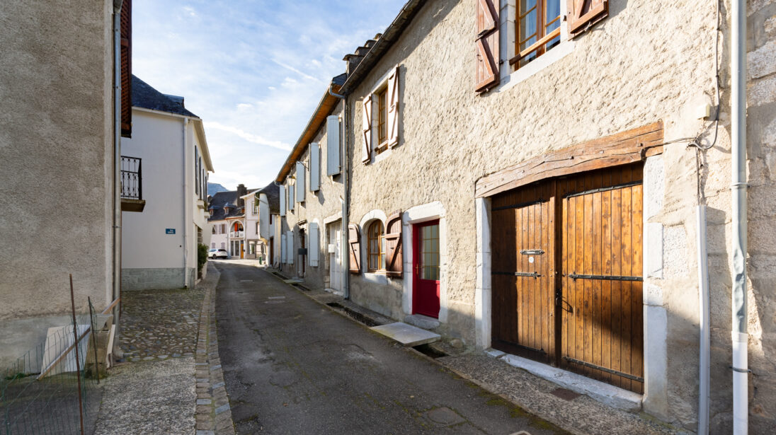 Ruelle pavée du village de Sarrancolin bordée de maisons en pierre avec porte de grange en bois