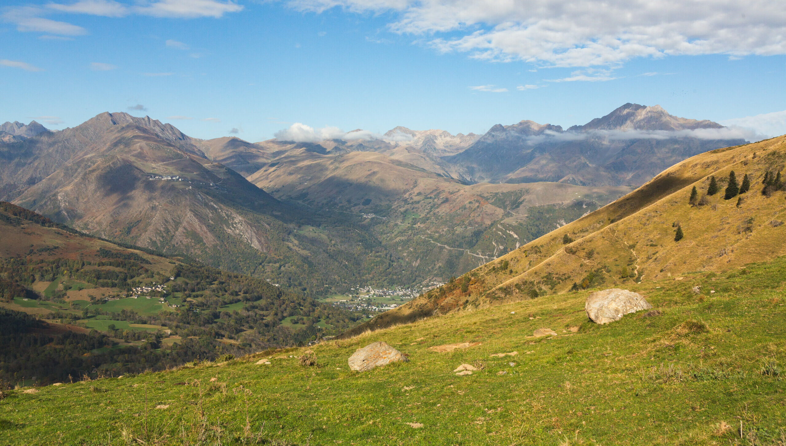 Vue panoramique sur la vallée du Louron avec village en fond de vallée et sommets pyrénéens à l'horizon