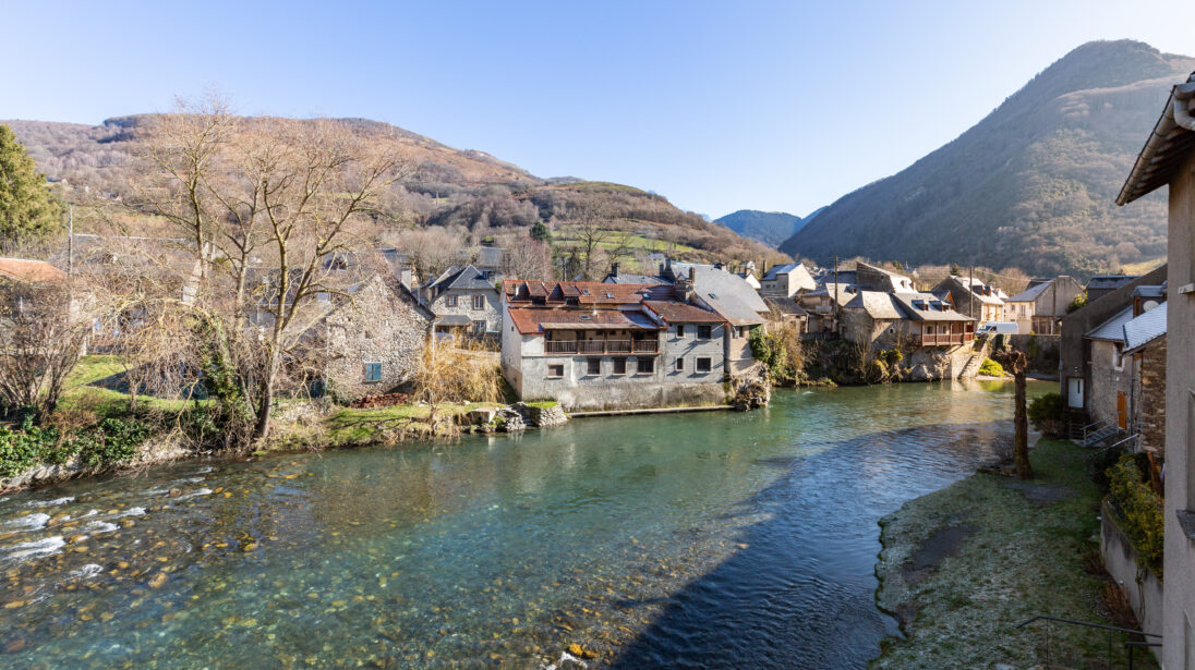 Vue sur le village de Sarrancolin traversé par la rivière la Neste, maisons en pierre et montagnes en arrière-plan